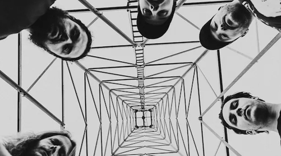 TRIBAL GAZE Announce New Album ‘Inveighing Brilliance’, Debut “Beyond Recognition” Video The Mosh Network -Tribal Gaze promotional photo 2025 with the band looking down at the lense under a cell phone tower.